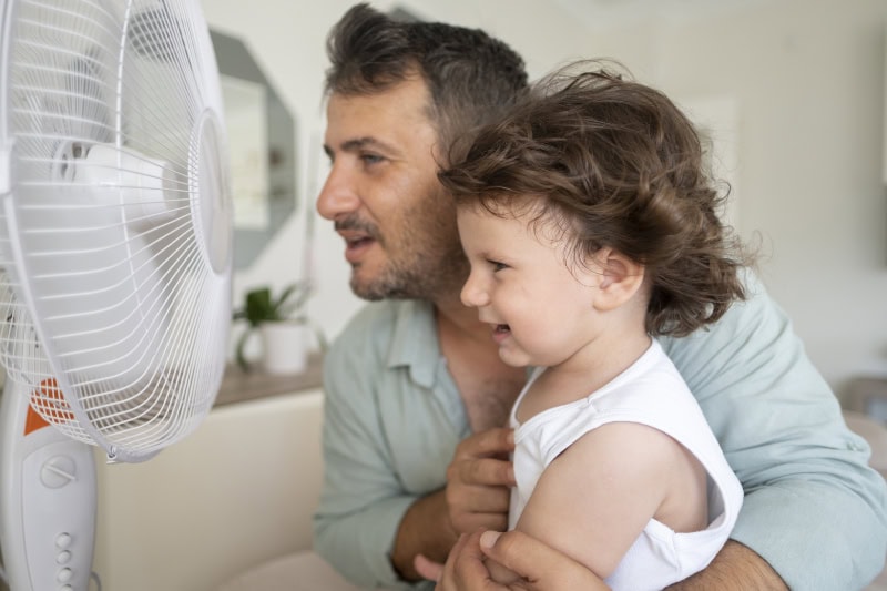 father and child sitting in front of a fan together.