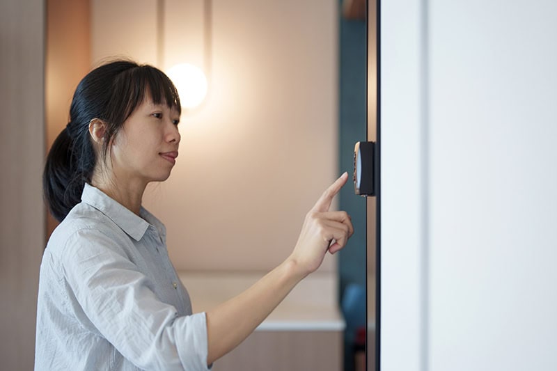 Woman adjusting thermostat mounted on the wall in her home.