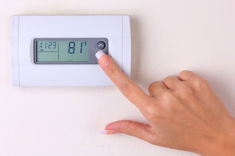 Someone adjusting a digital thermostat mounted on the wall.